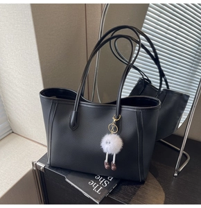 Dettaglio borsa tote in pelle nera con un divertente ciondolo mostro di pelliccia bianca