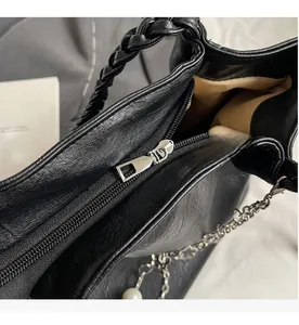 Detail view of the smooth silver zipper closure and woven handle with pearl chain decor