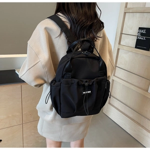 Detail of a lightweight black nylon backpack showing the drawstring pocket and back view