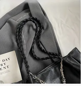 Detail of black tote bag featuring woven handle and floral metal chain on grey blazer