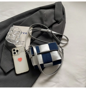 Close-up of woven crossbody bag in silver and navy on a grey blazer setting