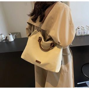 Close-up of beige canvas tote bag with brown leather handles and adjustable shoulder strap