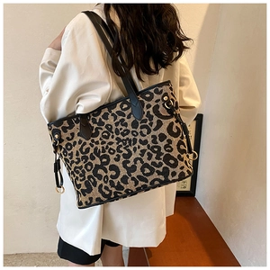 Detailed view of leopard print tote bag with black leather handles on model's shoulder