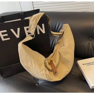 Close-up of khaki nylon crescent bag with leather puller on a leather sofa
