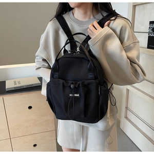 Side view of a woman wearing a black nylon backpack with drawstring front pocket