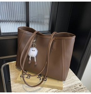 Dettaglio borsa tote in pelle marrone scuro con ciondolo di peluche e tracolla fine