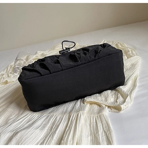 Detail of black pleated nylon shoulder bag with drawstring closure on soft white fabric