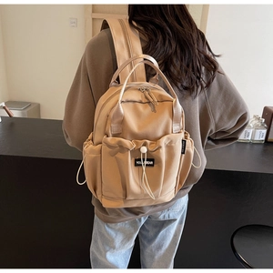 Detail of khaki nylon backpack featuring a drawstring front pocket and woven brand label