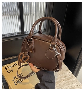 Detail of coffee leather handbag featuring white contrast stitching and heart charm accessory
