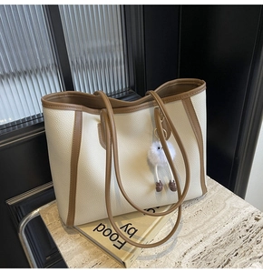 Dettaglio della borsa tote in pelle litchi bianco crema con bordi marroni e pompon