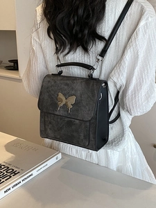 Sac à dos vintage gris foncé chic avec fermoir papillon doré porté sur une blouse blanche