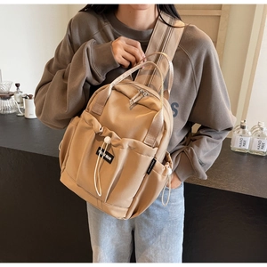 Close-up of lightweight khaki nylon backpack featuring front drawstring pocket and brand label