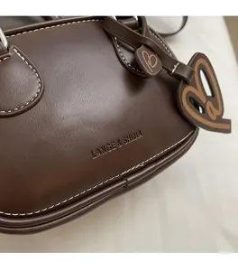Close-up of dark brown leather bowling bag with white stitching and heart pendant