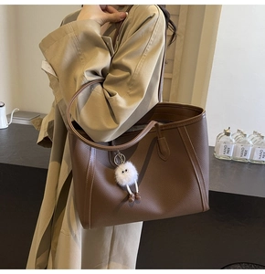 Dettaglio borsa tote marrone caffè in pelle martellata con ciondolo in peluche su trench beige