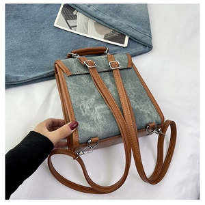 Detail of grey denim backpack featuring brown leather straps and silver metal buckles