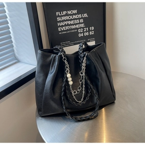 Detail of black pleated tote bag featuring woven handles and silver chain with pearls