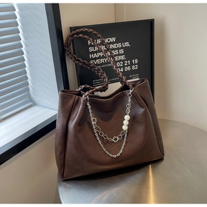 Detail of dark brown tote bag with woven handles and pearl chain charm on metal table