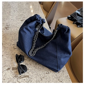 Detail of blue denim tote bag with chain strap on marble surface with sunglasses