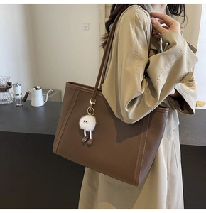 Borsa tote marrone scuro con trama in pelle e ciondolo a mostro sulla spalla di una modella