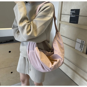 Detail of light pink nylon crescent crossbody bag worn by a model in a minimalist setting
