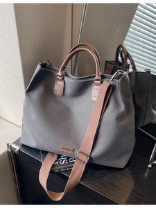 Grey nylon tote bag with brown leather handles and adjustable shoulder strap for daily commute