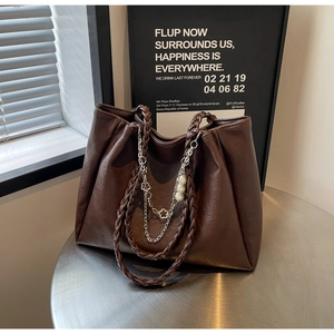 Detail of dark brown tote bag with woven handles, silver chains, and pearl flower charms