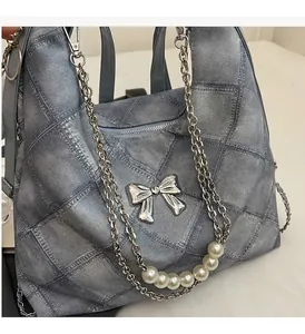 Detail of blue denim tote bag featuring silver bow hardware and pearl chain strap