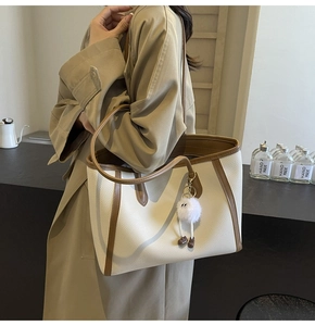 Modella che indossa una borsa tote bianco sporco con bordi marroni e ciondolo di peluche
