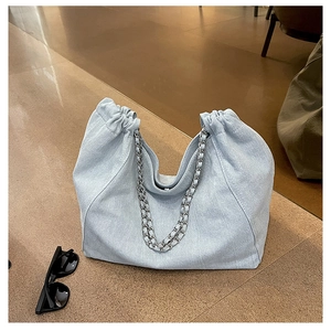 Detail of light blue denim tote bag with silver chain strap and gathered top design