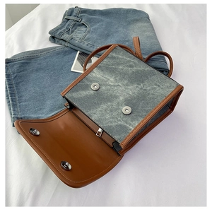 Detail view of square flap bag with gray vintage denim texture and brown leather piping
