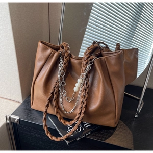 Close-up of brown textured leather tote bag with woven handles and floral pearl chain