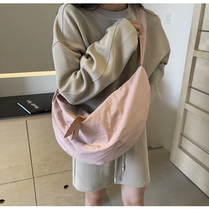 Detail showing pink crescent nylon crossbody bag worn on shoulder with brown zipper puller
