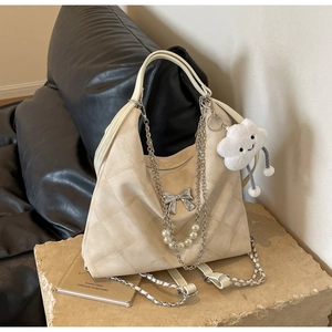 Close-up of cream quilted tote bag with silver bow accent and pearl chain detail