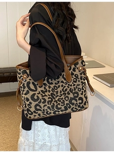 Large leopard print tote bag with brown leather handles worn by model in casual setting