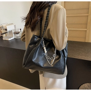 Detail of black leather tote bag with braided strap and pearl chain charm on model