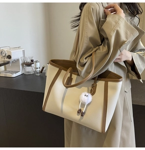 Vista dettagliata della borsa tote beige con finiture in pelle marrone e ciondolo a orsetto