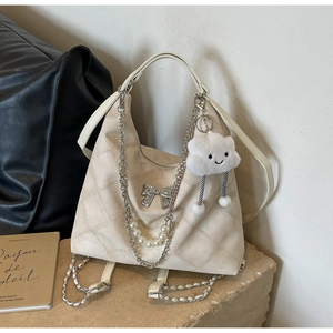 Close-up of beige quilted tote with silver bow charm, pearl chain, and plush cloud pendant