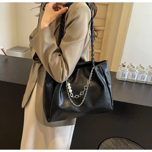 Close-up of black leather tote with woven strap, silver chains and pearl charms
