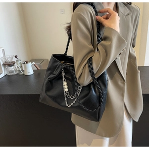 Detail of black tote bag with woven straps and decorative pearl flower metal chain