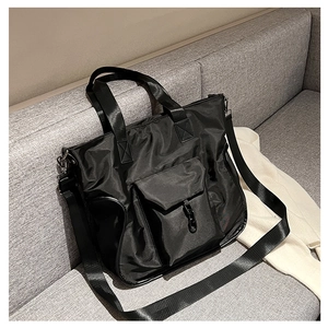 Close-up of black nylon tote bag with front pocket and adjustable strap on a sofa
