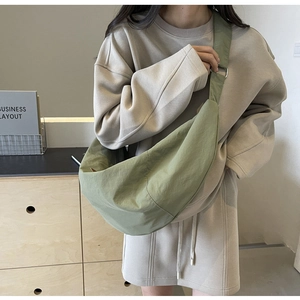 Olive green nylon dumpling bag shown on a shoulder in a casual lifestyle setting