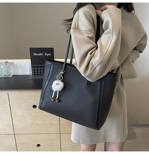 Dettaglio della borsa tote in pelle nera con ciondolo a mostro bianco portata dal modello