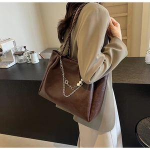 Detail of dark brown vintage tote bag with metal chains and pearl charms on woven strap