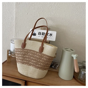 Detail of handwoven straw tote bag with brown leather handles on wooden cabinet