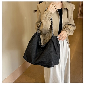 Detail of black denim tote bag with thick silver chain strap worn by a female model