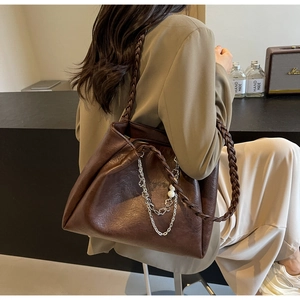 Detail of dark brown tote bag featuring woven straps, silver chain and pearl accents