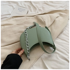 Détail du sac selle vert clair avec chaîne argentée posé sur un blazer beige