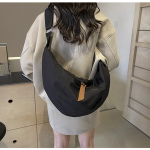 Detail of adjustable strap and silver metal buckle on black nylon crescent crossbody bag