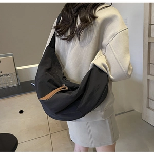 Detail of a large black nylon crescent bag worn crossbody with brown leather zipper pull