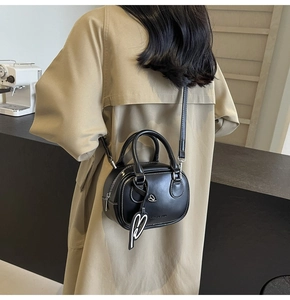 Detailed view of a black bowling bag featuring a heart charm shown on a beige coat back